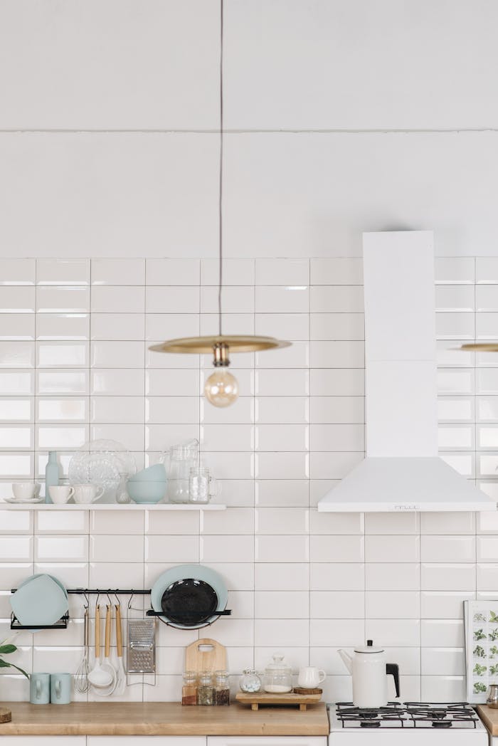 Bright and modern kitchen with white tiles, shelves, and a stylish light fixture.