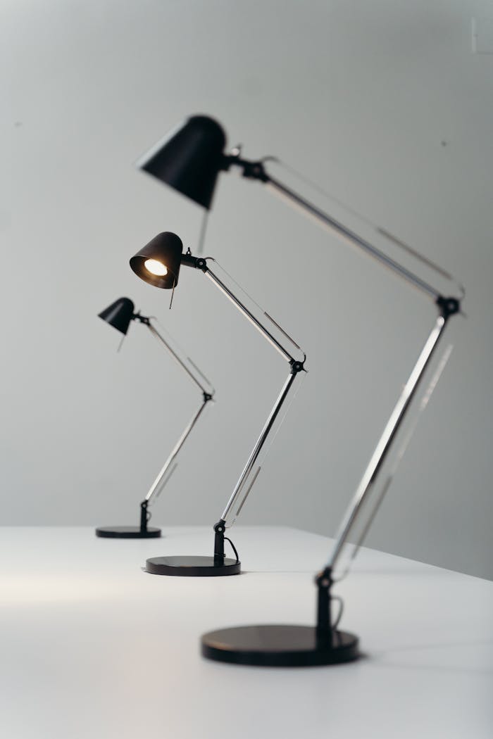 Three modern black desk lamps on a white desk against a gray background, showcasing sleek design.